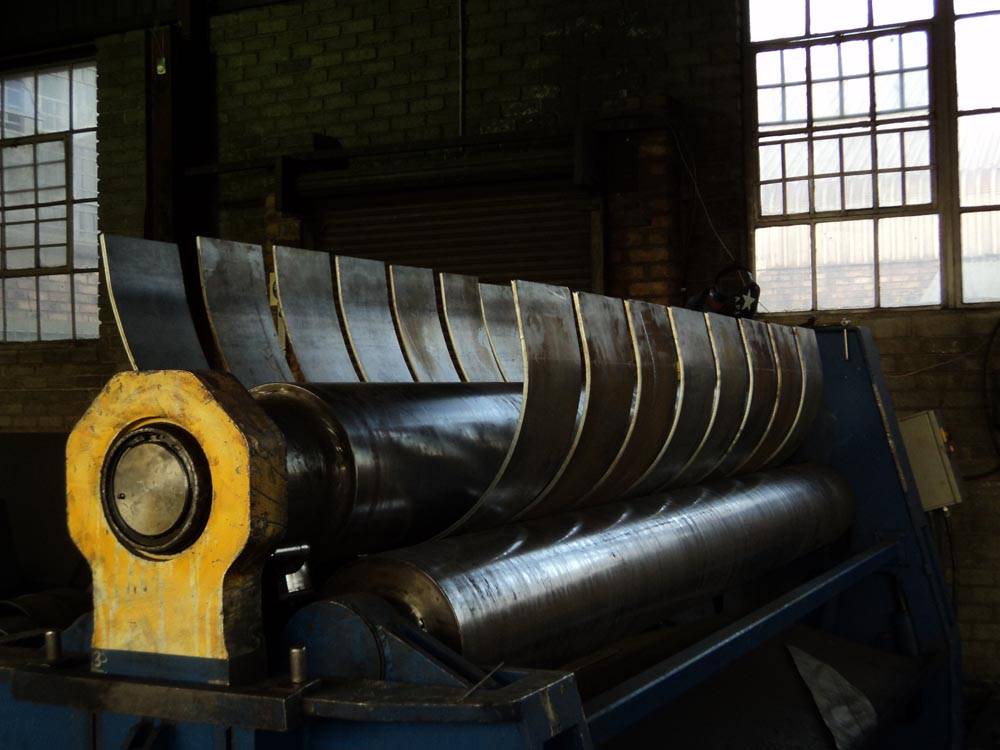 Industrial machine rolling multiple steel plates into curves